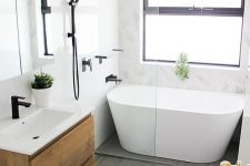 a laconic Scandinavian bathroom with white marble and grey stone tiles, an oval tub, a floating vanity, black fixtures and greenery