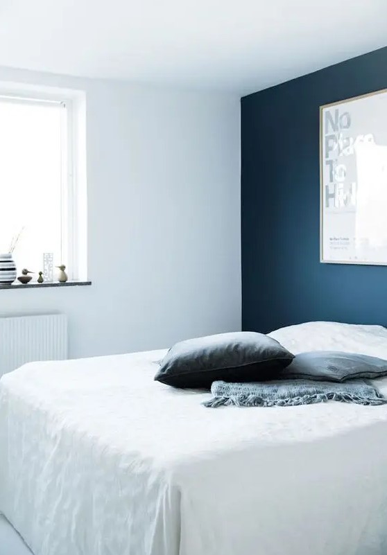 a laconic bedroom with a navy accent wall, a white bed with navy pillows and some decor on the windowsill