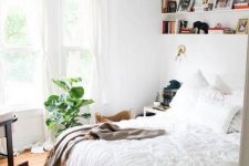 a light-filled bedroom with a bow window, some shelves, a bed with neutral bedding, potted plants is welcoming