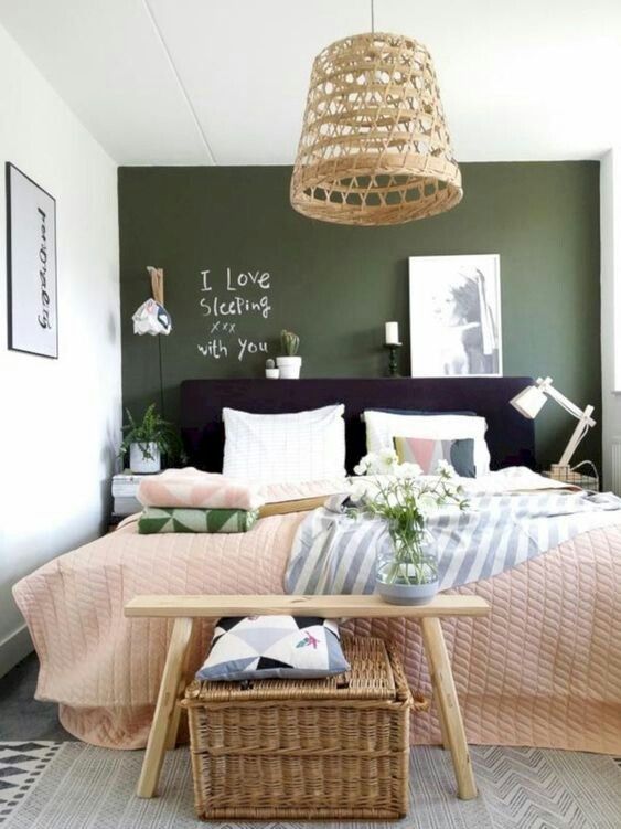 a lively bedroom with a green wall, a black bed, neutral and printed bedding, a bench, a woven chest and woven pendant lamp