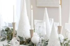 a lovely Christmas tablescape with white bottle brush trees, white candles in wooden candleholders, wooden placemats, white houses and fresh eucalyptus