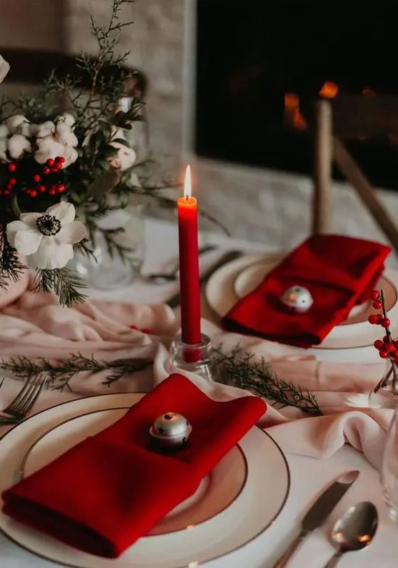 A lovely holiday tablescape with a blush runner, white blooms and red berries, red napkins and candles, simple gold rimmed plates