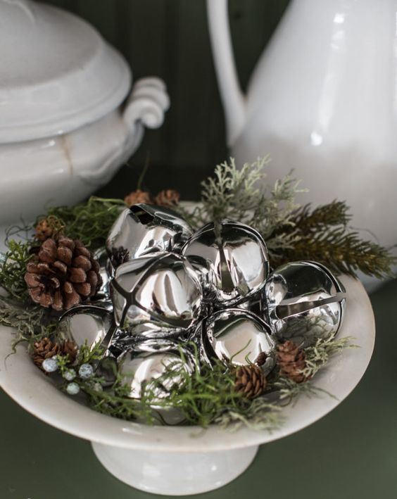 a lovely rustic Christmas centerpiece of a bowl with greenery, pinecones and silver bells is a cool last minute idea to go for
