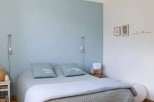 a minimalist bedroom with a blue accent wall, a bed with blue and grey bedding, a rug and a quirky pendant lamp
