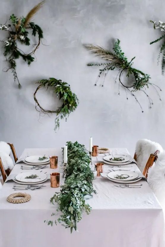 a minimalist tablescape with a lush greenery garland, copper touches and greenery wreaths on the wall