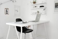 a minimalist white workspace with a white desk, a shelving unit, artworks and a little stool by the desk