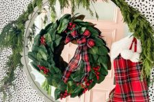 a mirror accented with a greenery, berry and plaid wreath, fir branches, a plaid stocking and plaid pillows for bright holiday decor