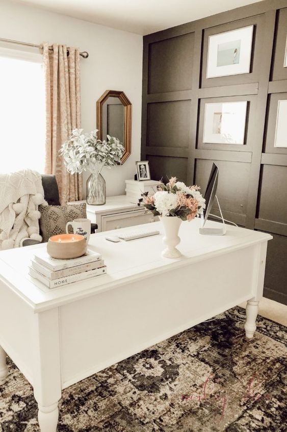 a modern farmhouse home office with a black panel wall, a vintage white desk, a boho rug, printed textiles and some blooms