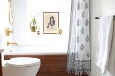a modern small bathroom with a penny tile floor, a wood clad bathtub, a rug, an artwork and gilded touches