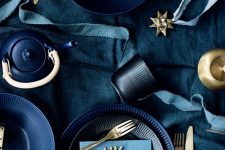 a moody blue and gold Christmas tablescape with gold cutlery, black and navy plates and blue linens for a a modern space