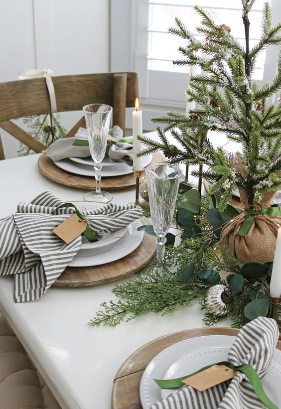 a natural Christmas table setting with greenery, fir, a Christmas tree in burlap, candles, metallic ornaments and striped napkins