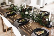 a natural Nordic Christmas table with a fir and pinecone runner, candles, black plates, bells, black candleholders