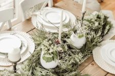 a neutral rustic Christmas table with white woven placemats, a greenery runner, tall candles and white porcelain