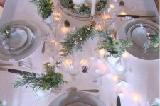 a neutral shiny Christmas tablescape with a centerpiece of candles and greenery, lights, flocked branches, mini ornaments and tall and thin candles