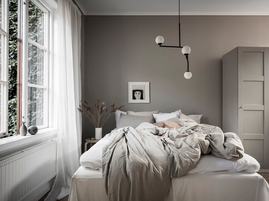 a peaceful grey Scandinavian bedroom with modern furniture, a catchy pendant lamp, some pretty vases and an artwork