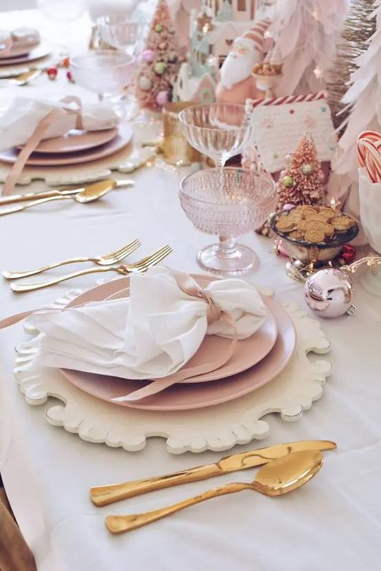 a pink Christmas tablescape with carved wooden placemats, pink plates, gold cutlery, pink Christmas trees, glasses and gingerbread houses