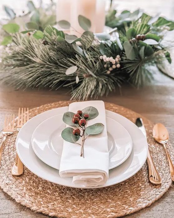 a pretty Christmas place setting with a woven placemat, white porcelain, evergreens and berries, gold cutlery is amazing