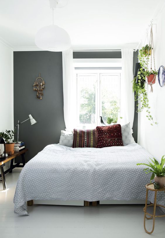 a pretty Scandinavian bedroom with a soot accent wall, a bed with printed bedding, potted greenery and a bench