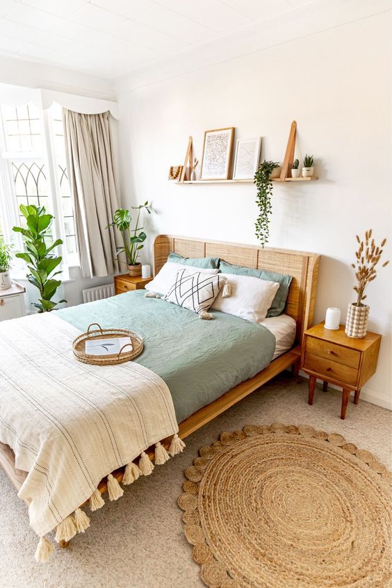 a pretty boho bedroom with a cane bed, stained nightstands, a boho rug, potted plants and some decor