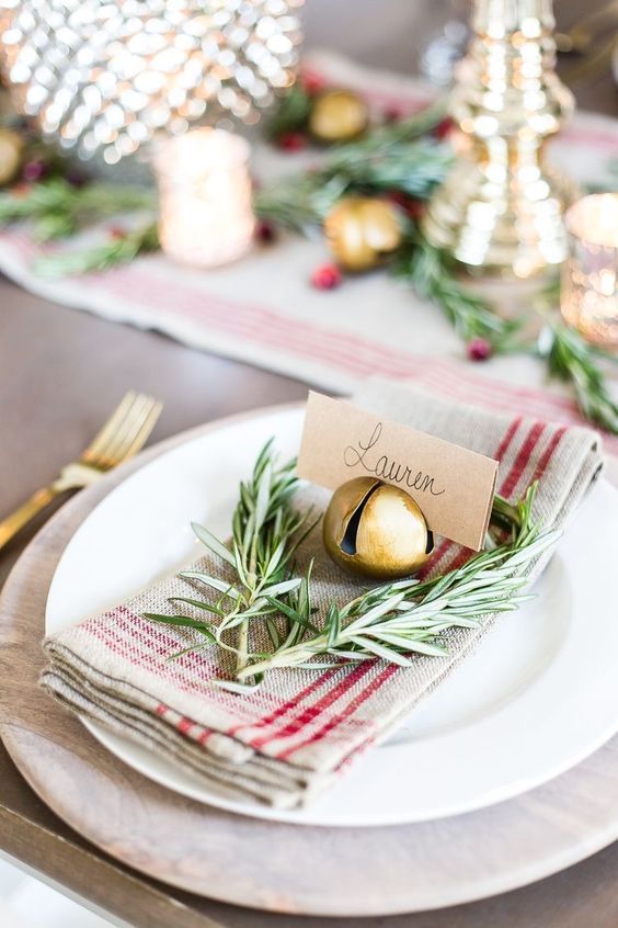 a pretty rustic Christmas place setting with a plaid napkin, greenery, a gold bell holding a card is very chic