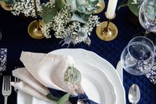 a refined Christmas tablescape with a navy tablecloth and bows, neutral napkins, greenery and white candles is a chic idea