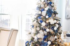 a refined and chic Christmas tree with lights, white and gold ornaments, fabric blooms and ribbons and twigs and branches