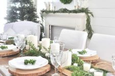 a rustic Christmas tablescape with an uncovered table, a greenery runner with candles, wood slice placemats
