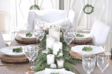 a rustic Christmas tablescape with wood slice chargers, an evergreen runner, candles and ornaments plus some greenery