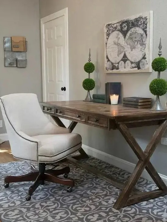 a rustic home office with a trestle desk, a printed rug, green topiaries, a white chair on casters is elegant