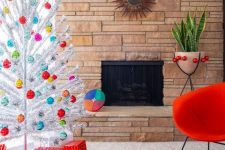 a silver Christmas tree with colorful ornaments and stacks of red gift boxes for a mid-century modern space