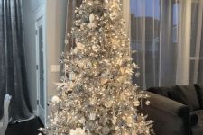 a silver Christmas tree with lights, white and silver ornaments, fabric blooms and silver gift boxes is a stylish and bold idea