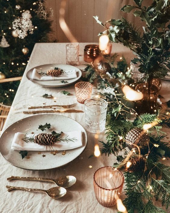 a simple Christmas setting with a fir branch runner, lights, candles, catchy glasses, pinecones, greenery and printed porcelain