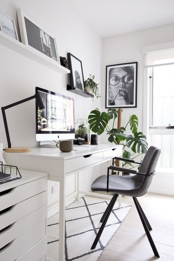 a small Scandinavian home office with a white desk, a storage unit, a grey chair, a ledge with artwork and a potted plant