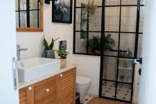 a small and catchy bathroom with white and black and white tiles, a shower space with black framing, a vanity, art and a mirror