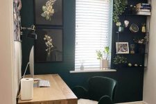 a small and cool home office with a black accent wall, a stained desk, a dark green chair, a shelving unit and some art