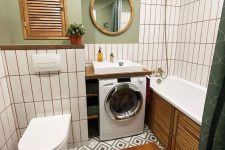 a small and cozy bathroom with green walls, white skinny tiles, a tub with a wooden screen, a washing machine and a mirror