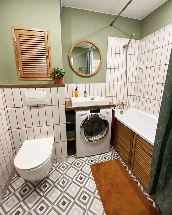a small and cozy bathroom with green walls, white skinny tiles, a tub with a wooden screen, a washing machine and a mirror