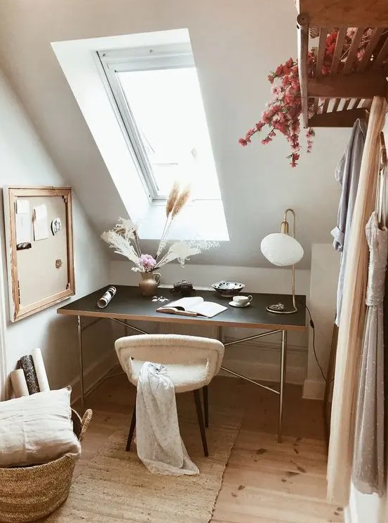 a small and lovely attic home office with a black desk by the skylight, a soft chair, a memo board, a basket with a pillow is cozy