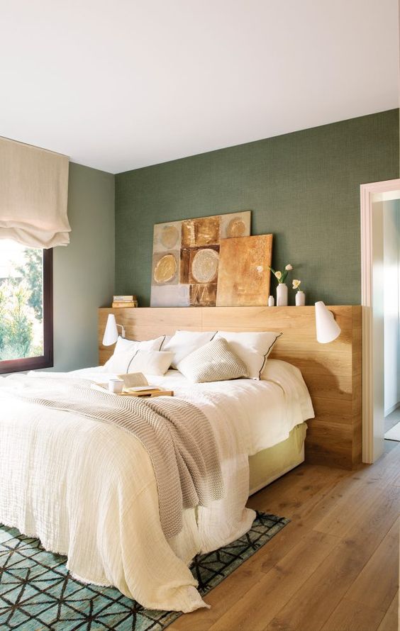 a small and lovely bedroom with green walls, a bed with a gallery wall, neutral bedding, a printed rug and neutral curtains