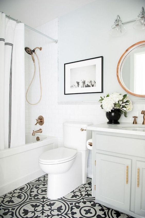 a small and pretty farmhouse bathroom with a black and white tiled floor, white tiles, a vintage vanity and a round mirror