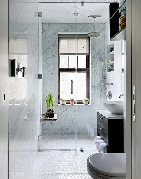a small bathroom with blue stone tiles in the shower, a dark stained vanity, potted greenery and built-in shelves