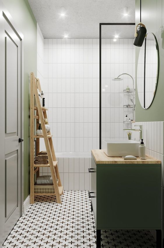 a small bathroom with green walls, skinny white tiles, printed ones, a bathtub, a green vanity, a round mirror and some lights
