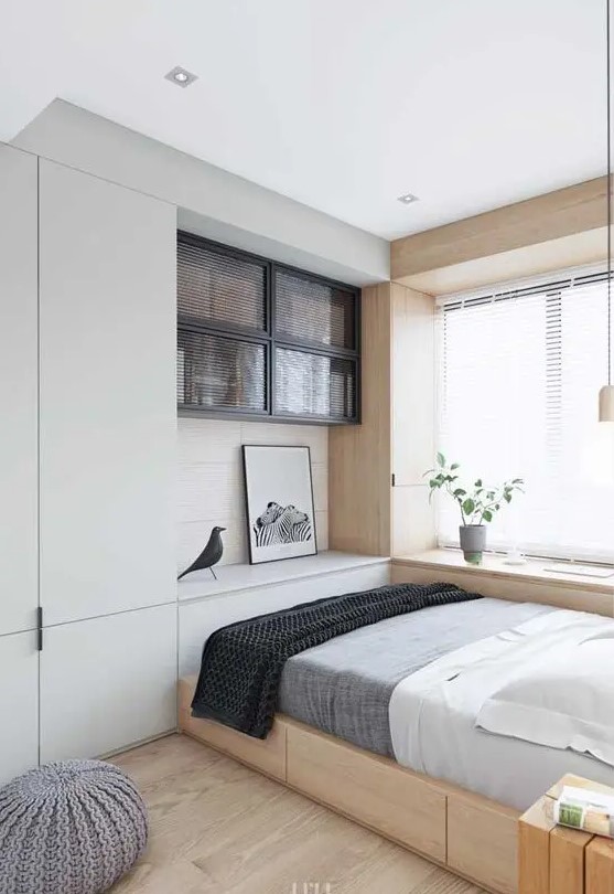 a small bedroom looks larger thanks to the neutral color scheme, a large window by the bed and floor to ceiling furniture