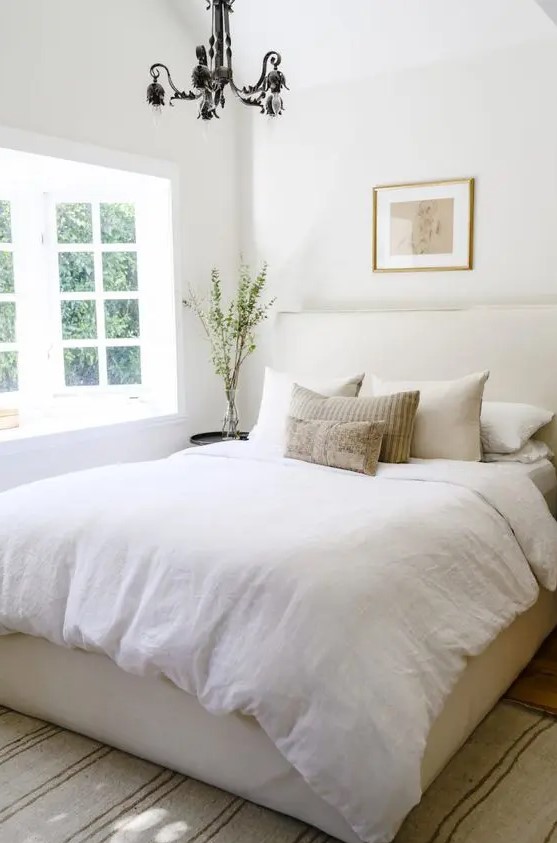 a small bedroom with a neutral color scheme and a bay window that brings much light inside looks bigger