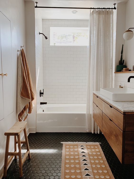 a small boho bathroom with white subway and black hex tiles, a stained vanity, a printed rug, black fixtures
