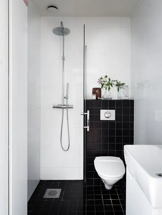 a small contrasting bathroom with black and white tiles, a shower space, a sink and greenery to refresh the look