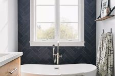 a small contrasting bathroom with navy herringbone tiles and white walls, a stained vanity, a tub next to the window and a wooden mat
