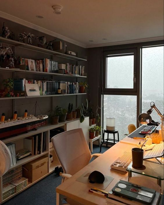 a small home office with a floor to ceiling window, open shelves, a storage unit, a desk, a chair and a table lamp