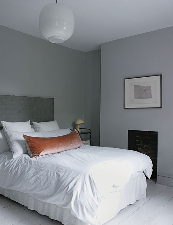 a small minimal bedroom with grey walls, a bed with neutral bedding, a fireplace and an artwork is lovely