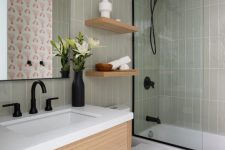a small modern bathroom with light green tiles, a stained vanity, black fixtures, a mirror and open shelves